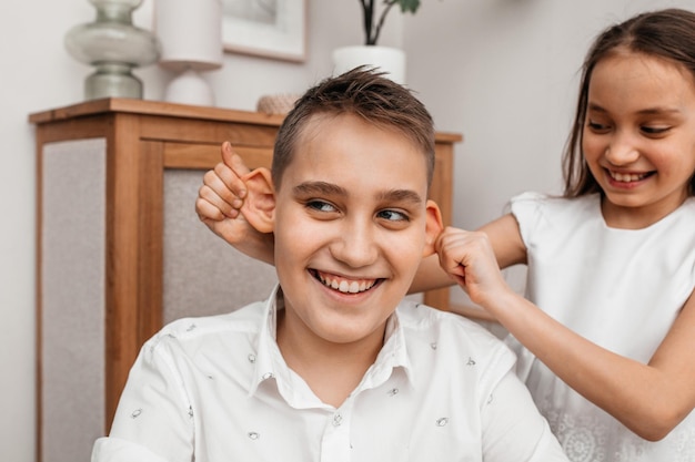 Foto de jongere broer en zus trekken grappige gezichten het meisje houdt de jongen bij de oren