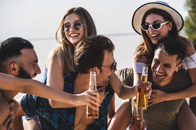 De jongeren met flessen genieten van de zomer op het strand