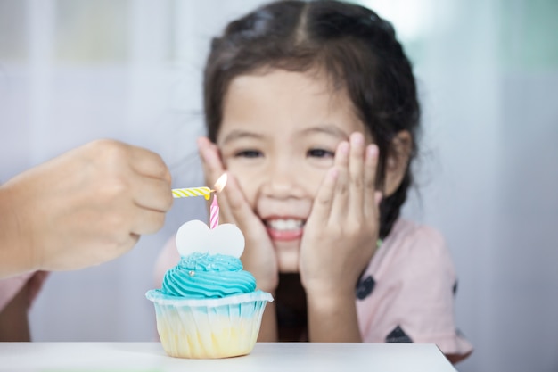 De kaars van de de handverlichting van de moeder op verjaardag cupcake voor kindmeisje vierend en blazende kaarsen op verjaardag