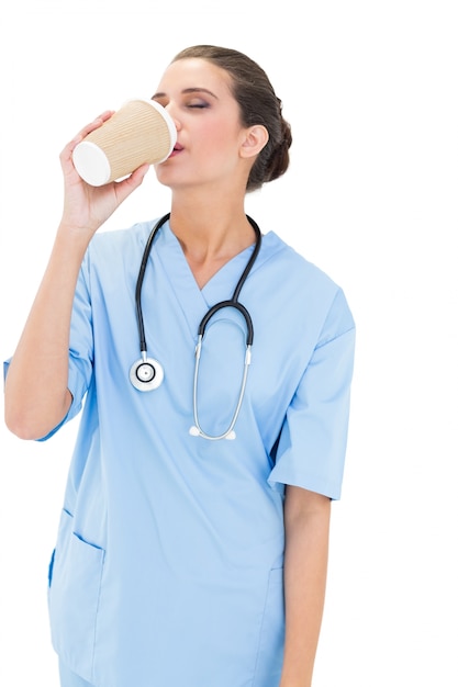 De kalme bruine haired verpleegster in blauw schrobt genietend van haar koffie