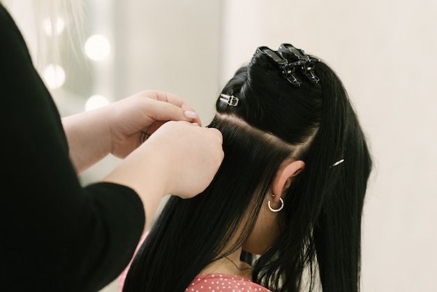 De kapper doet haarextensies aan een jong meisje in een schoonheidssalon. Professionele haarverzorging.