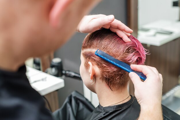 De kapper gebruikt kam voor vrouwelijk roze haar bij schoonheidssalon.