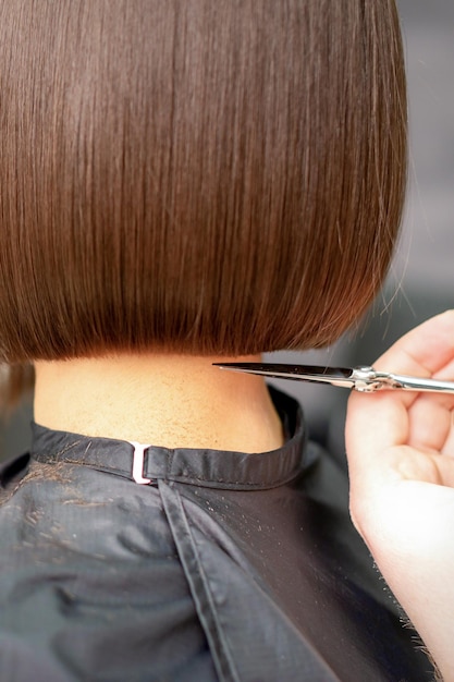 De kapper knipt het haar van een brunette vrouw. Haarstylist knipt het haar van een vrouwelijke klant in een professionele kapsalon, close-up.