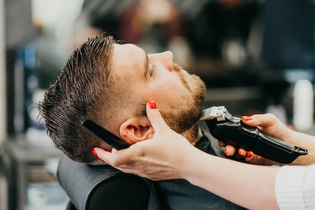De kapper snijdt zijn baard aan een brutale man in de salon
