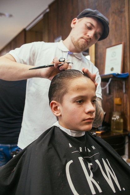 De kapper van de kapsels van de tiener in de kapper. Modieus stijlvol retro kapsel. Portret van een kind met een mooi kapsel.