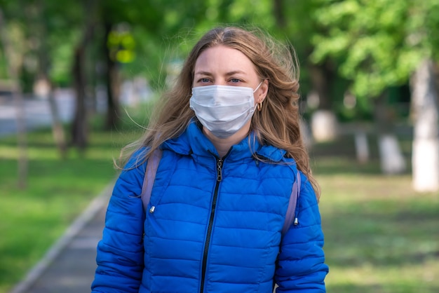 De Kaukasische blondevrouw in beschermend masker en handschoenen loopt langs lege straat. Veilig gedrag tijdens pandemie