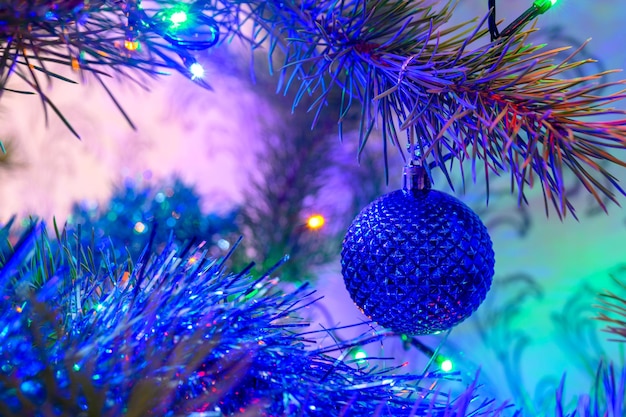 De kerstbal op een kerstboom tegen de achtergrond van wazige lichten van een slinger