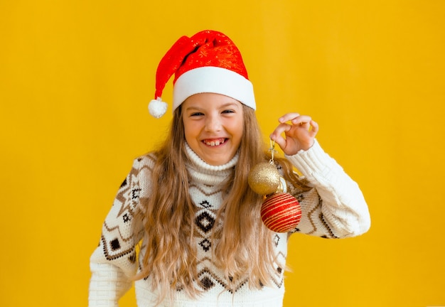 De kerstboom versieren. klein blond meisje met kerstballen. kind in een nieuwjaarshoed heeft nieuwjaarsversieringen.