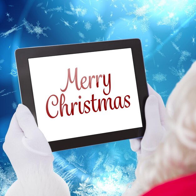 Foto de kerstman die tabletpc met behulp van tegen het blauwe patroonontwerp van de sneeuwvlok
