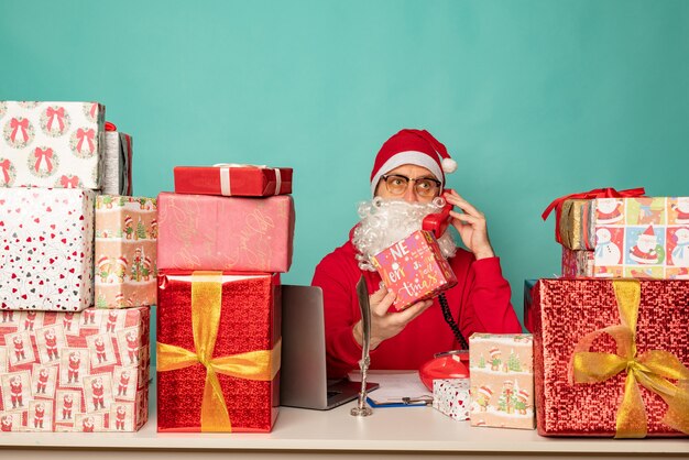 De kerstman draagt hoedenwerk in zijn kantoor met cadeautjes en bereidt zich voor op vakantie.