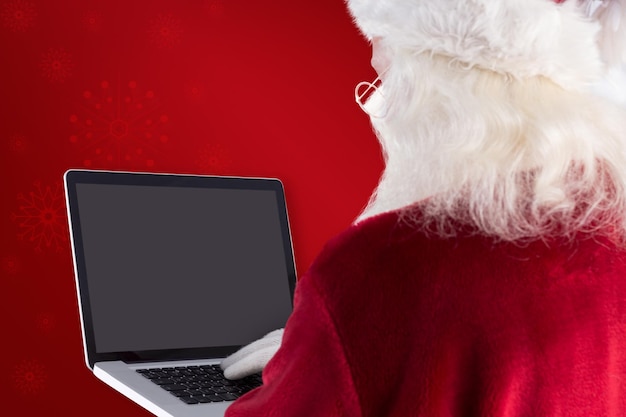 De Kerstman gebruikt laptop tegen rode achtergrond