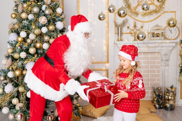 De kerstman geeft een babymeisje een cadeau bij de kerstboom