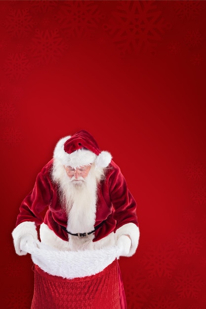De kerstman kijkt in zijn tas tegen een rode achtergrond