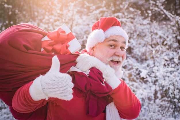 De kerstman komt met duim omhoog in het sneeuwbos senior duimen omhoog teken