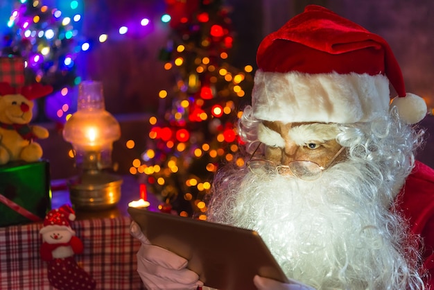 De kerstman leest 's avonds een boek in huisHet licht uit het boekHet licht uit de lantaarnkamer gebruikenE-book lezen van tablet