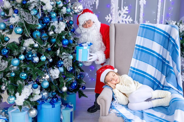 De kerstman legt een cadeau onder de boom terwijl het kind slaapt