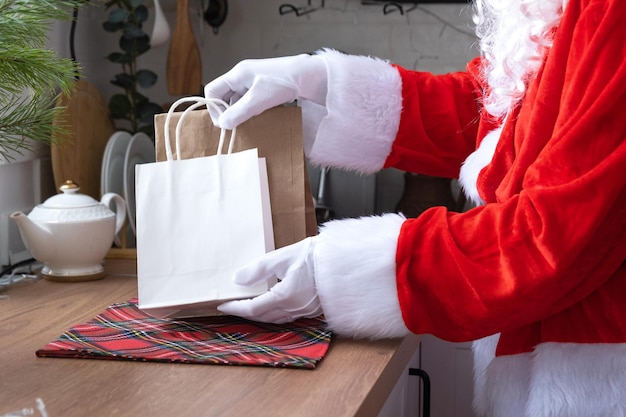 De kerstman legt het op de keukentafel en haalt papieren zakken weg met ambachtelijk cadeau, zelfgemaakt gebak en voedselbezorging Winkelverpakkingen recycling handgemaakte bezorging voor Kerstmis en Nieuwjaar