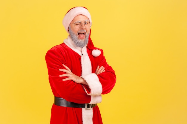 De kerstman met een positief gezicht kijkt naar de camera en knipoogt, houdt de mond open.