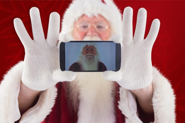 Foto de kerstman neemt zichzelf op met een smartphone tegen een rode achtergrond