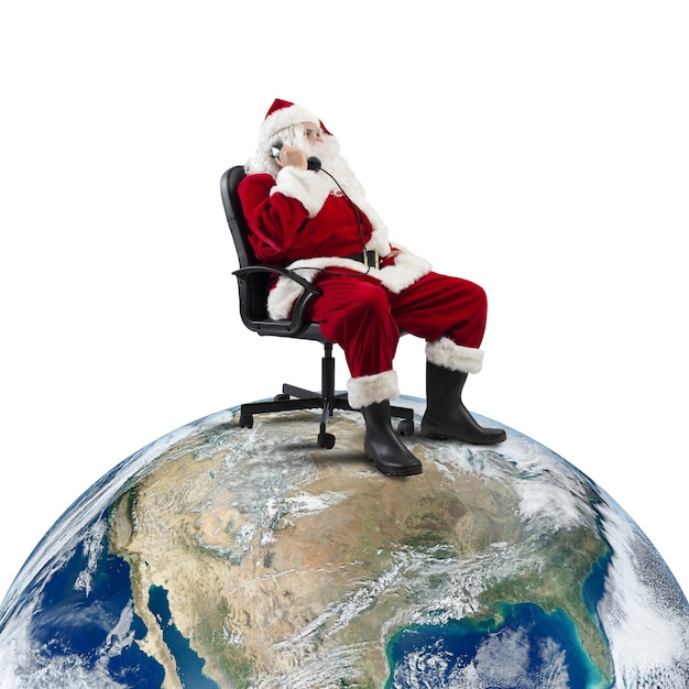 De kerstman ontvangt verzoeken via de telefoon zittend in een stoel op een grote wereld