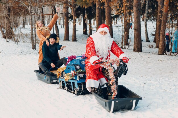 De kerstman rijdt op een verliefd sneeuwscooterpaar in het winterbos