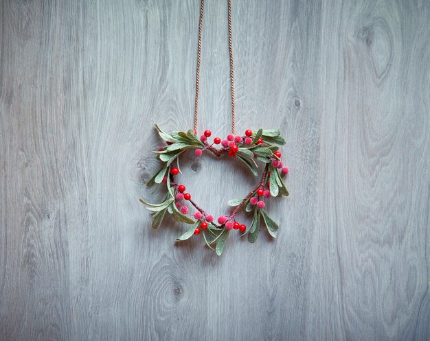 De Kerstmiskroon in een vorm van maretak met rode bessen hangt op rustieke geweven houten deur