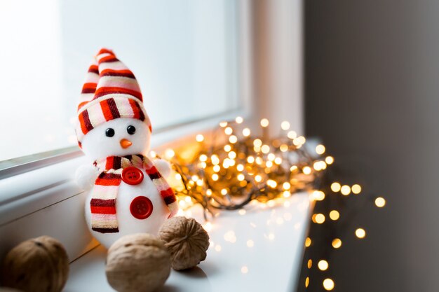 De Kerstmissneeuwman en de okkernoten liggen op het venster op de achtergrond van de slinger van het Nieuwjaar