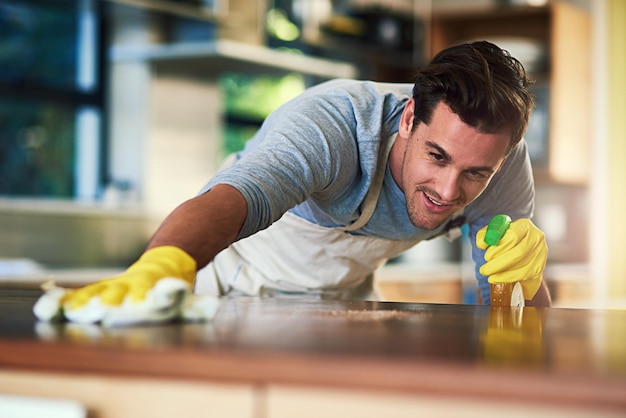 De keuken zal binnenkort sprankelend schoon en brandschoon zijn Bijgesneden opname van een jonge man die thuis een keukenoppervlak schoonmaakt