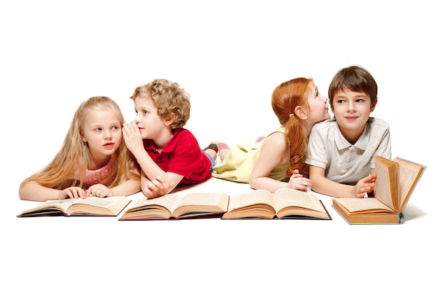 De kinderen jongen en meisjes leggen met boeken in de studio, glimlachen, lachen, geïsoleerd op wit. Dag van boek, onderwijs, school, kind, kennis, jeugd, vriendschap, studie en kinderen concept