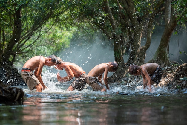 De kinderen van Azië op rivier / het gelukkige gelukkige grappige speelwater van de jongensvriend in de waterstroom in platteland