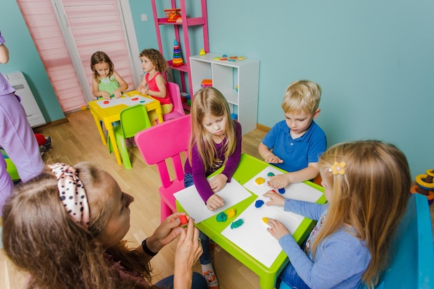 De kinderen zitten aan de bureaus en beeldhouwen uit plasticine de kinderen met opvoeders ontwikkelen creativiteit op de kleuterschool