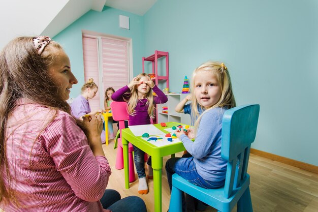 De kinderen zitten aan de bureaus in de kleuterschool en beeldhouwen verschillende figuren met plasticine