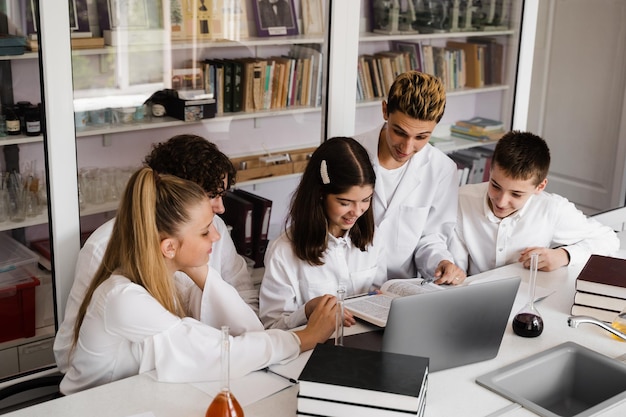 De klas studeert in de scheikundeles op school in het laboratorium Onderwijs De leraar controleert het huiswerk in het boek Voorbereiding op experimenten