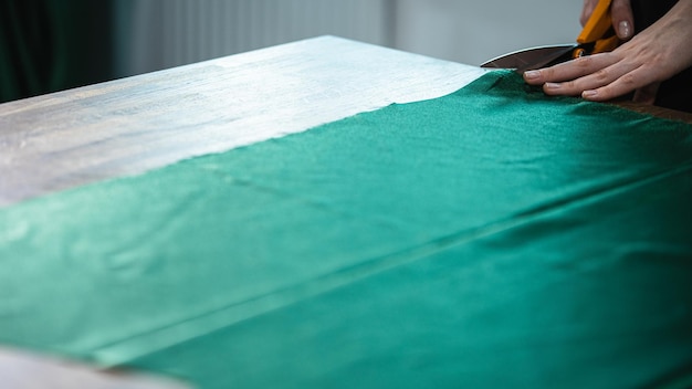 De kleermaker knipt de groene doek op tafel met een schaar.