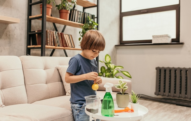 De kleine helperjongen zit op de bank en plant planten aan de tafel in de kamer