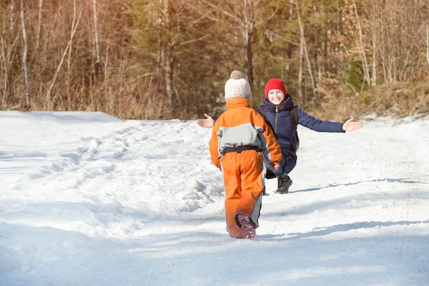 De kleine jongen in overall loopt door de sneeuw naar de moeder winterdag in het naaldbos achteraanzicht