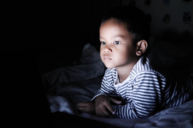 De kleine jongen keek 's nachts in het donker naar het scherm van de laptop