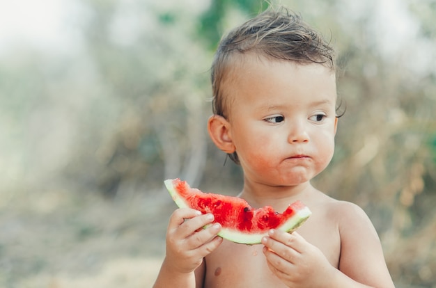 De kleine jongen, zonder shirt, watermeloen aan het eten terwijl hij op vakantie is