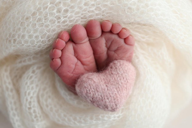 Foto de kleine voet van een pasgeboren baby de zachte voeten van een nieuwgeboren baby in een witte woldeken close-up van de tenen, hielen en voeten van de pasgeboren baba een gebreide roze hart in de benen van een baby macrofotografie
