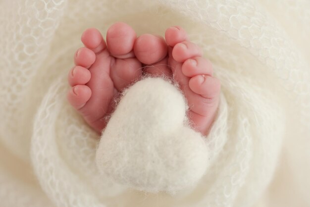De kleine voet van een pasgeboren baby Zachte voeten van een pasgeborene in een witte wollen deken Close-up van tenen, hakken en voeten van een pasgeborene Gebreid wit hart in de benen van een baby Macrofotografie