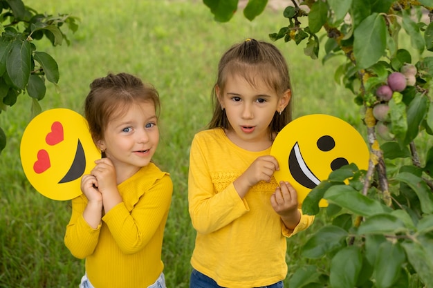 De kleine zusjes houden de gezichten van vrolijke emoticons in hun handen