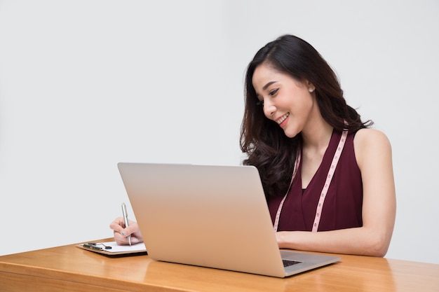 De kleren van de de manierontwerper van de vrouw in rode kleding met het meten van band en laptop geïsoleerde computer, Aziatisch vrouwelijk modieus model