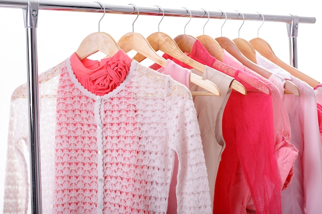 De kleren van roze vrouwen op houten hangers op rek op witte achtergrond. kast vrouwen jurken, blouses