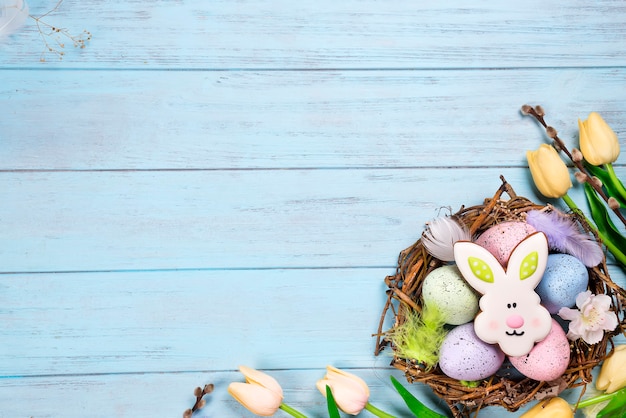 De kleurrijke Pasen-koekjes van het eijpeind als konijn in het nest met tulpen op houten achtergrond