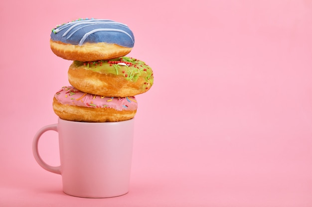 De kleurrijke samenstelling van het donutsontbijt met verschillende kleurenstijlen van donuts en verse koffie op roze achtergrond