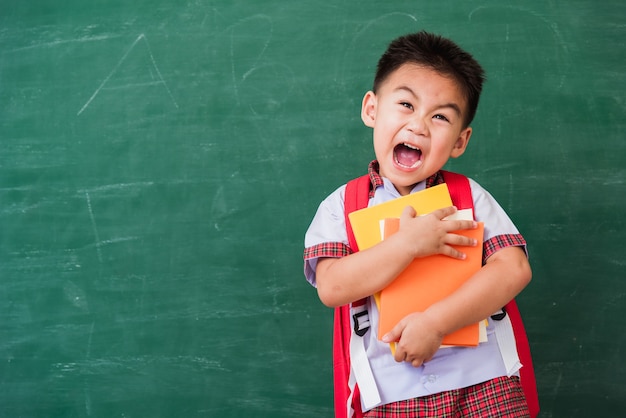 De kleuterschool van de kleine kindjongen in studentenuniform met schooltasgreep of knuffelboeken