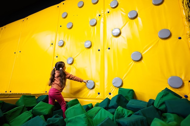 De klimmuur van het kleine meisjejonge geitje bij geel speelplaatspark Kind in beweging tijdens actief amusement