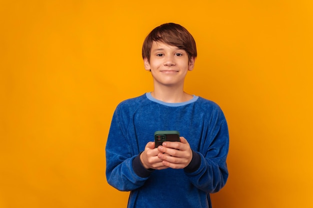 Foto de knappe glimlachende tienerjongen houdt een telefoon en bekijkt de camera