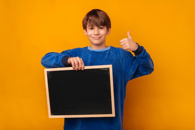 De knappe jonge jongen die blauw draagt houdt een leeg bord en een duim omhoog