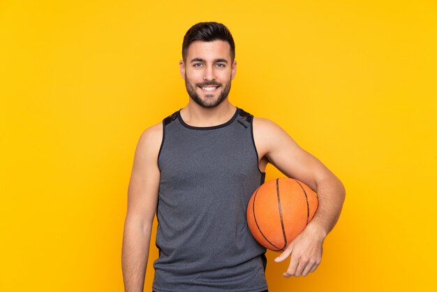 De knappe jonge mens van de basketbalspeler over geïsoleerde witte muur die heel glimlacht